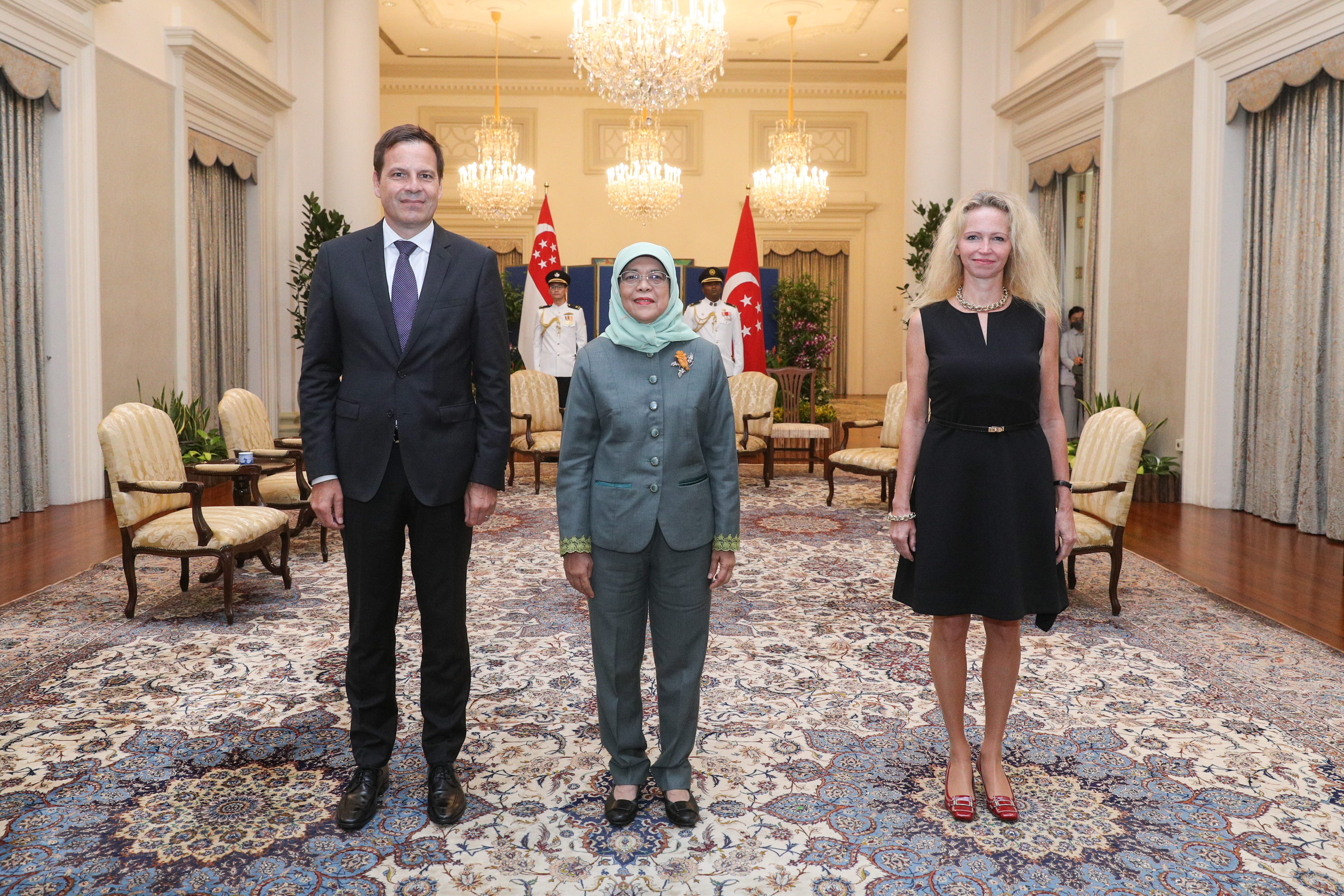 Three people posing in a room with chandeliers and Singapore flags behind them.